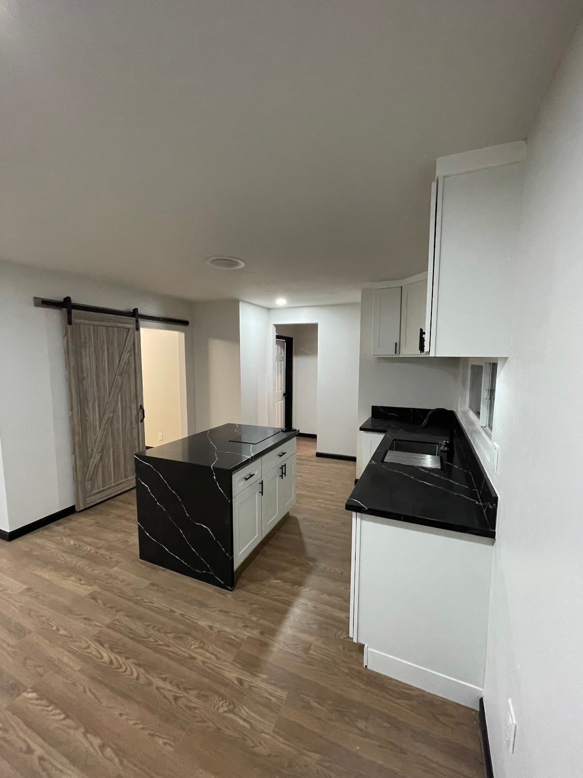 Modern kitchen featuring black marble countertops, white cabinets, wood floors, and a barn door.
