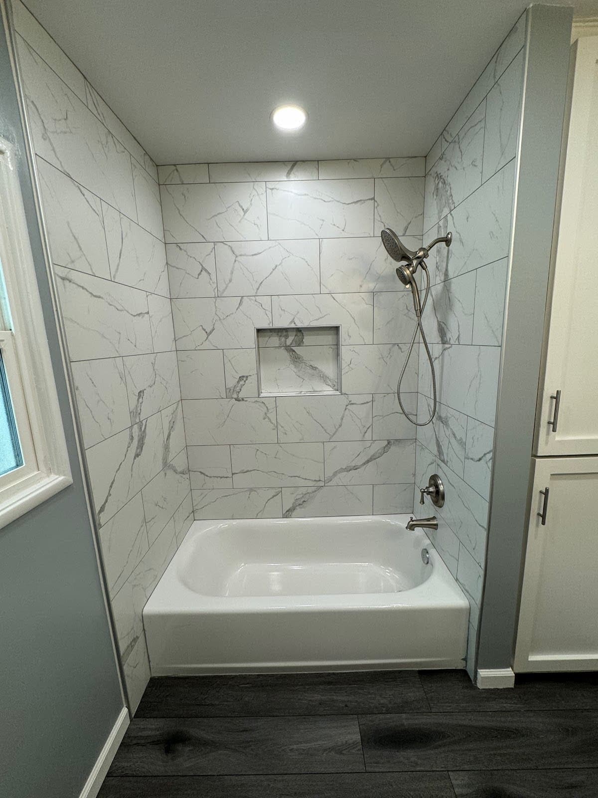 Modern white bathtub with marble-patterned tile walls, a recessed niche, and brushed nickel hardware.