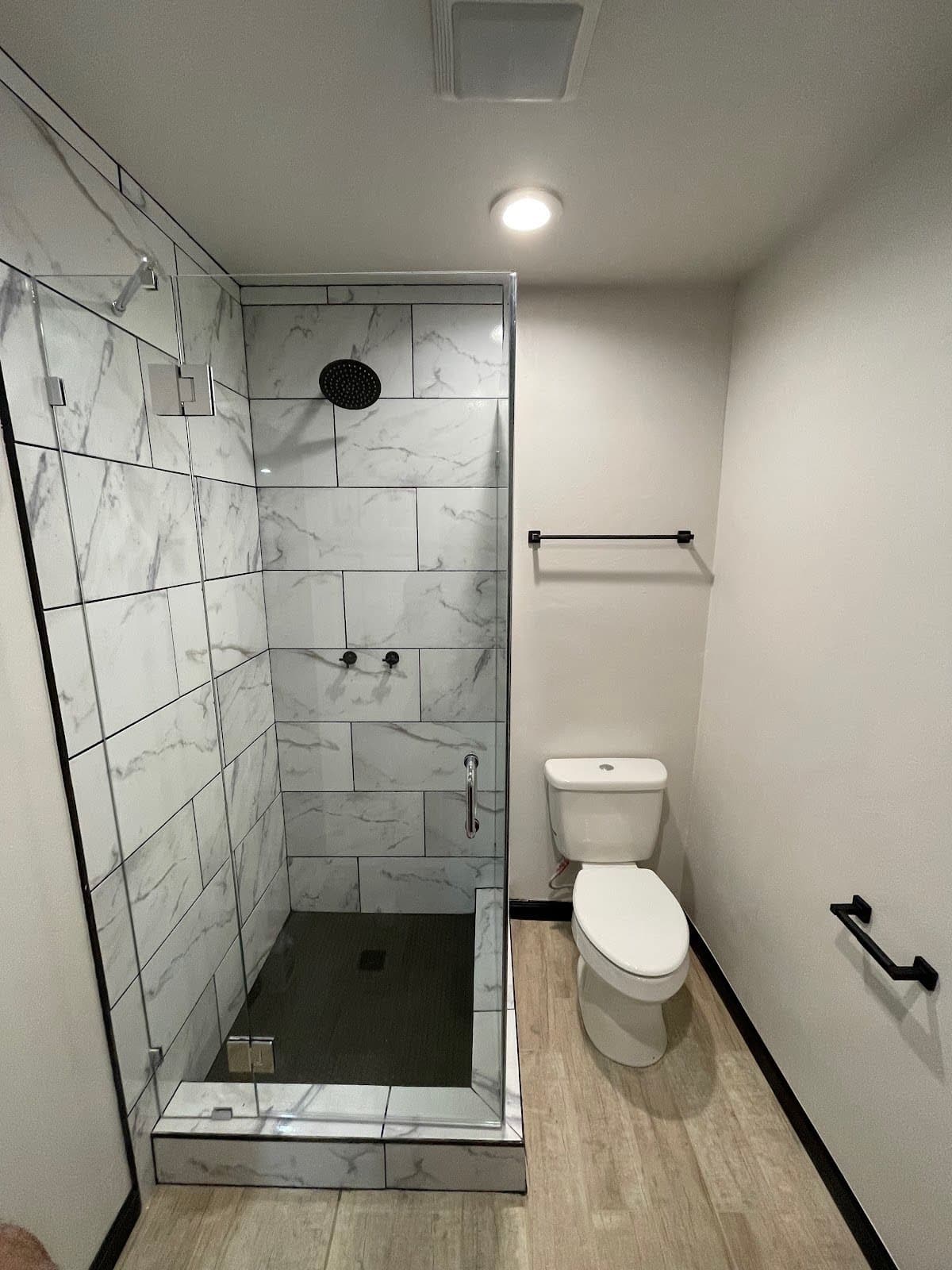 Modern bathroom with a marble tiled glass shower, black fixtures, and a white toilet.