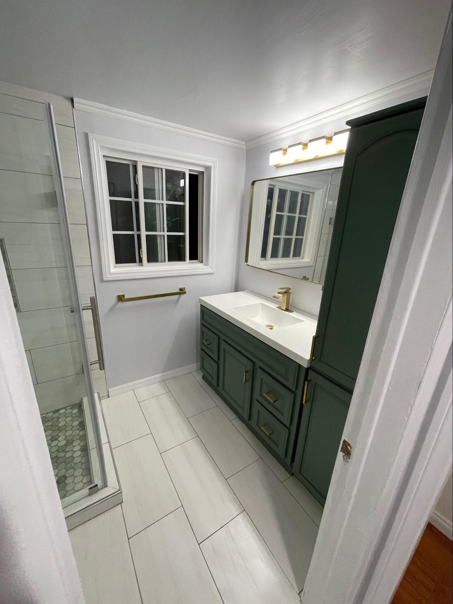 Modern bathroom featuring green cabinetry, gold hardware, white tile floors, and a glass shower.